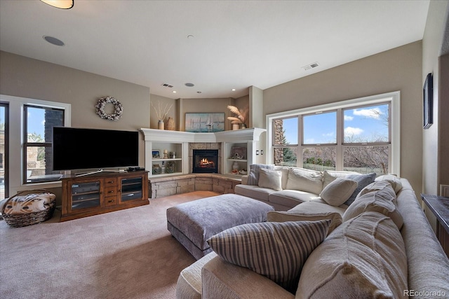 living area with a healthy amount of sunlight, carpet, a stone fireplace, and visible vents