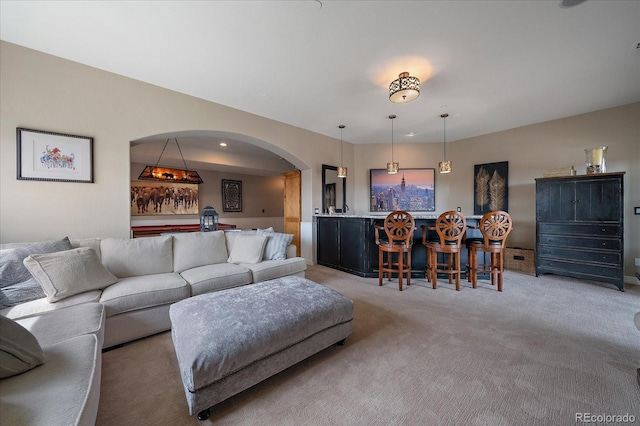 living area with a dry bar, light colored carpet, and arched walkways