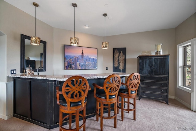 bar with hanging light fixtures, light carpet, indoor wet bar, and baseboards