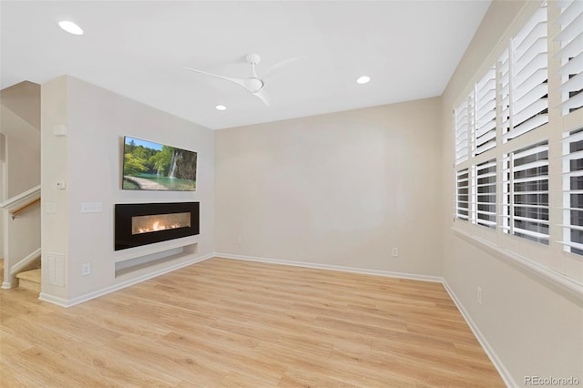 unfurnished living room with a glass covered fireplace, recessed lighting, baseboards, and wood finished floors