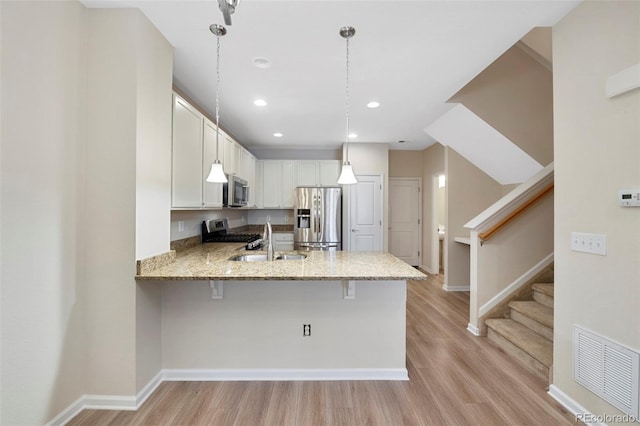 kitchen with visible vents, light stone countertops, appliances with stainless steel finishes, a peninsula, and a sink