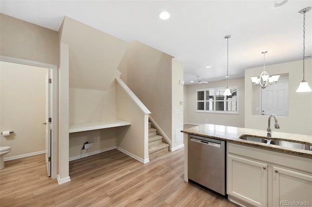 kitchen featuring light wood finished floors, light stone counters, stainless steel dishwasher, an inviting chandelier, and a sink