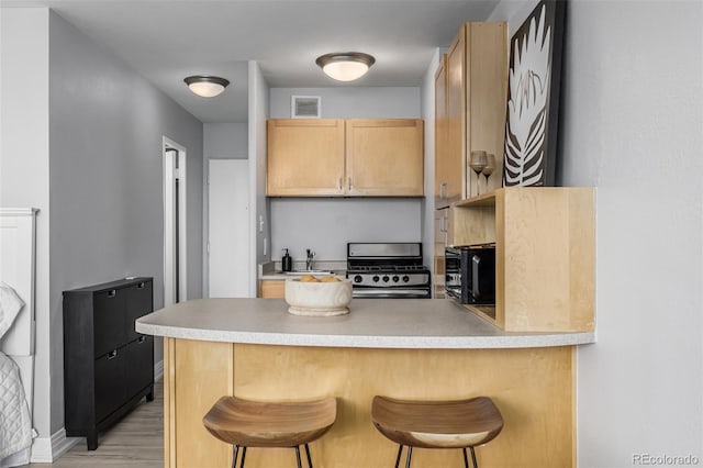 kitchen featuring sink, a kitchen breakfast bar, light hardwood / wood-style floors, light brown cabinetry, and stainless steel range with gas cooktop