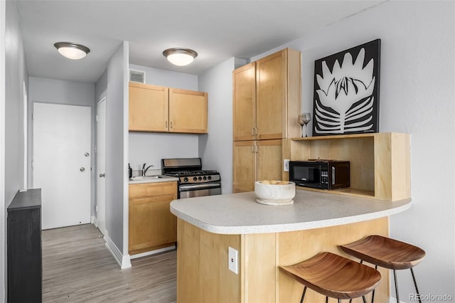 kitchen featuring stainless steel range with gas cooktop, light brown cabinetry, sink, kitchen peninsula, and light hardwood / wood-style flooring