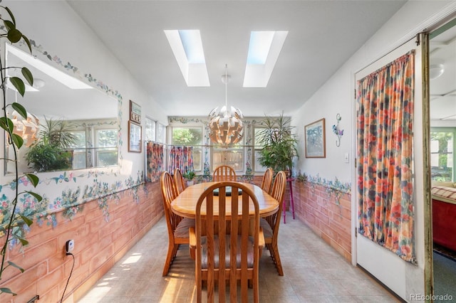 dining room featuring a chandelier, a skylight, plenty of natural light, wainscoting, and light tile patterned floors