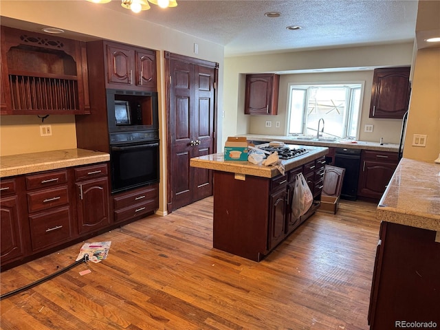 kitchen with light wood-style floors, a sink, a kitchen island, and black appliances