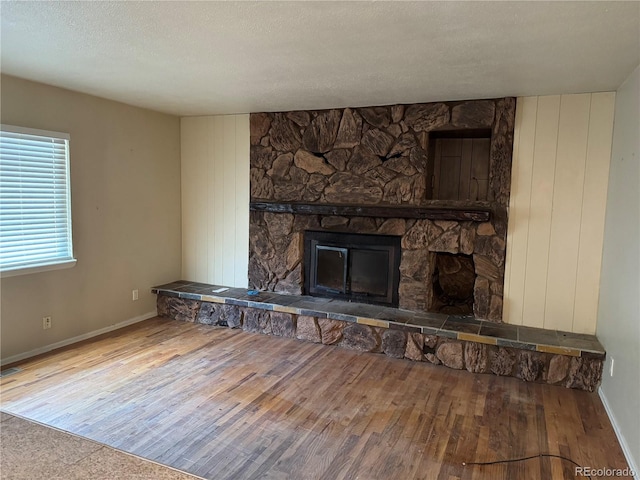 unfurnished living room with a textured ceiling, baseboards, wood finished floors, and a stone fireplace