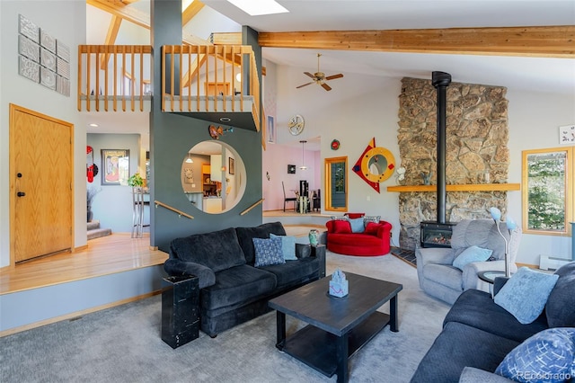 carpeted living area with ceiling fan, stairs, high vaulted ceiling, a wood stove, and beam ceiling