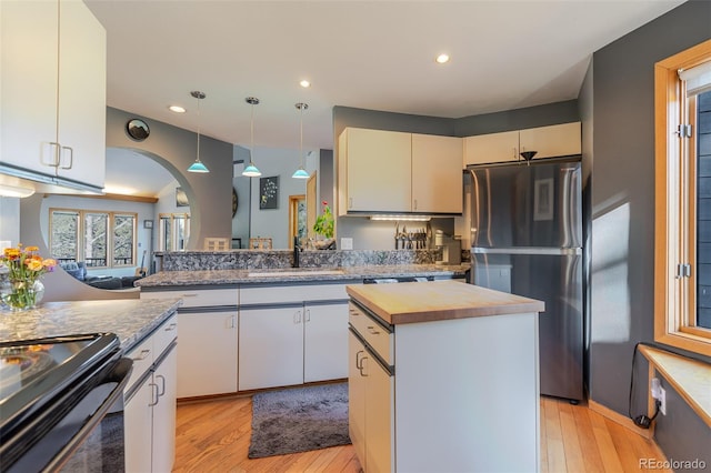 kitchen featuring freestanding refrigerator, butcher block countertops, pendant lighting, a sink, and light wood-style floors