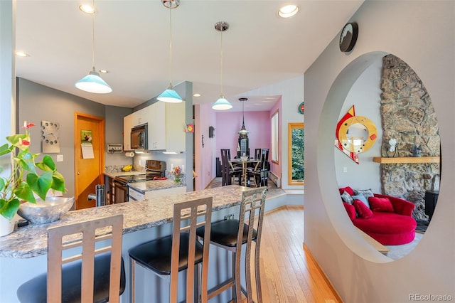 kitchen with light stone counters, black microwave, electric stove, light wood-style floors, and white cabinets