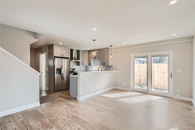 kitchen with appliances with stainless steel finishes, backsplash, pendant lighting, wall chimney exhaust hood, and kitchen peninsula