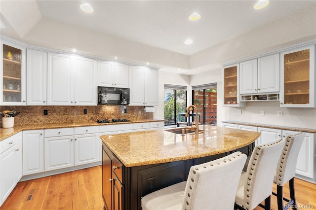 kitchen featuring light stone countertops, black appliances, white cabinetry, an island with sink, and sink