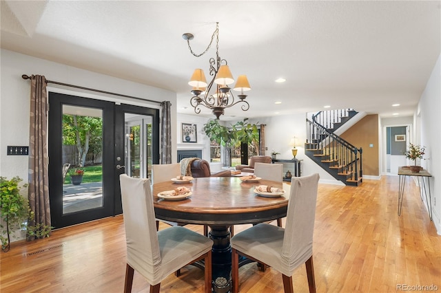 dining area with light wood-type flooring, french doors, and an inviting chandelier