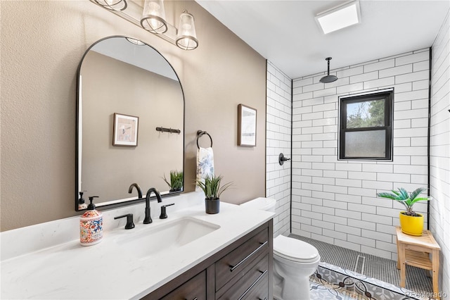 bathroom with toilet, tiled shower, and vanity