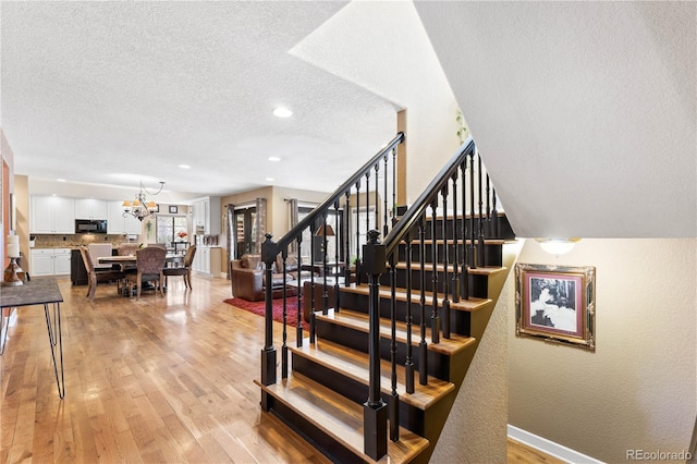 staircase with wood-type flooring, a textured ceiling, and a chandelier