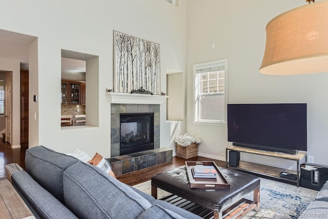 living room featuring a tile fireplace, a towering ceiling, baseboards, and wood finished floors