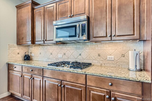 kitchen with light stone counters, stainless steel appliances, baseboards, backsplash, and brown cabinetry