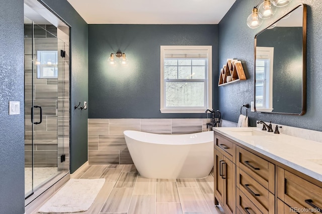 bathroom featuring double vanity, a stall shower, a textured wall, a freestanding tub, and a sink