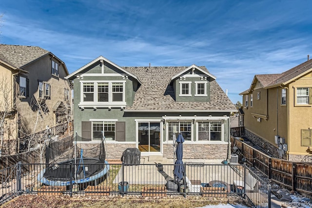 back of property with stone siding, a trampoline, a patio area, and a fenced backyard