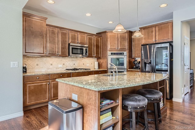 kitchen featuring light stone counters, hanging light fixtures, appliances with stainless steel finishes, decorative backsplash, and dark wood-style floors