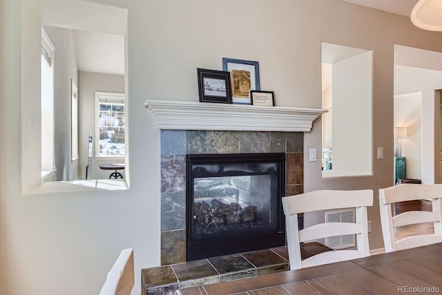 living area featuring visible vents, a tiled fireplace, and wood finished floors