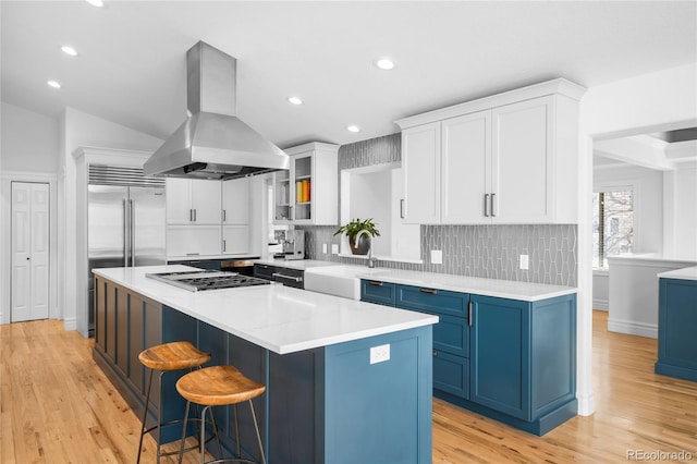 kitchen with a kitchen island, blue cabinets, island exhaust hood, gas stovetop, and a sink