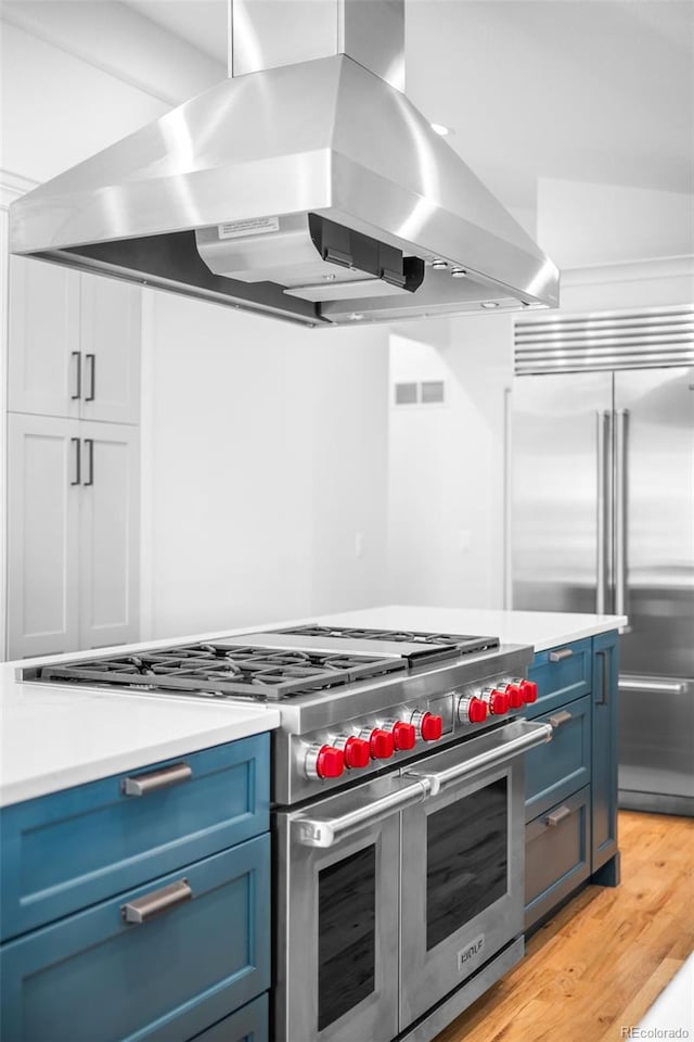 kitchen featuring light wood-style flooring, blue cabinets, light countertops, high end appliances, and island exhaust hood