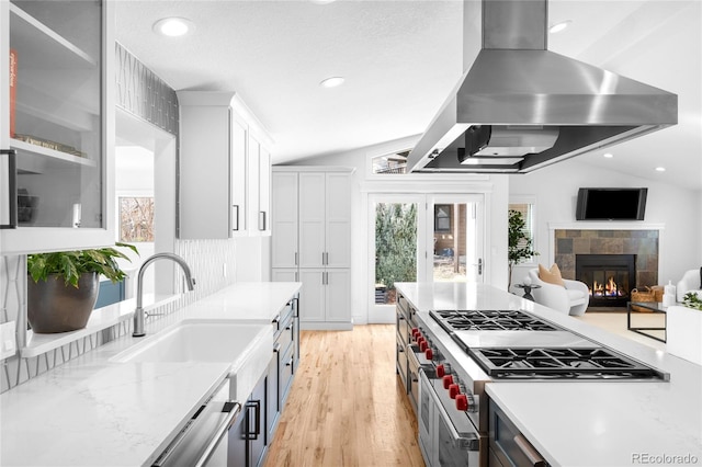 kitchen with white cabinets, vaulted ceiling, wall chimney range hood, and a sink