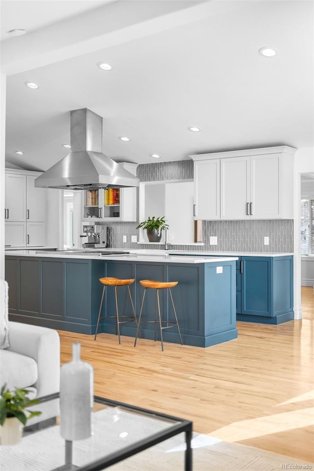 kitchen featuring tasteful backsplash, light wood-style floors, white cabinets, and island range hood