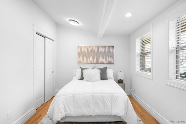 bedroom with a closet, beamed ceiling, light wood-style flooring, and baseboards