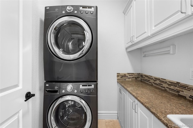 clothes washing area featuring stacked washer / drying machine, cabinet space, and baseboards