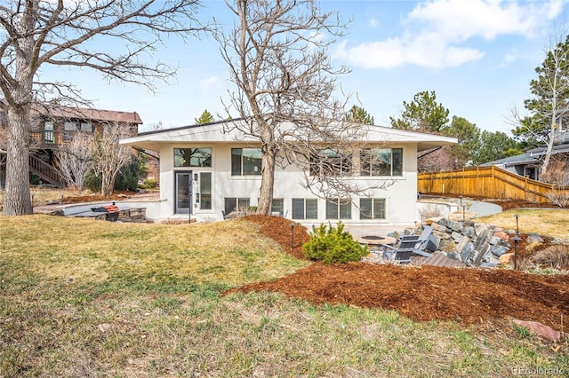 rear view of house with stucco siding, a lawn, a patio, and fence