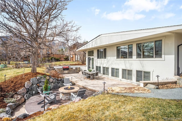 rear view of house featuring an outdoor fire pit, a patio, a lawn, and stucco siding