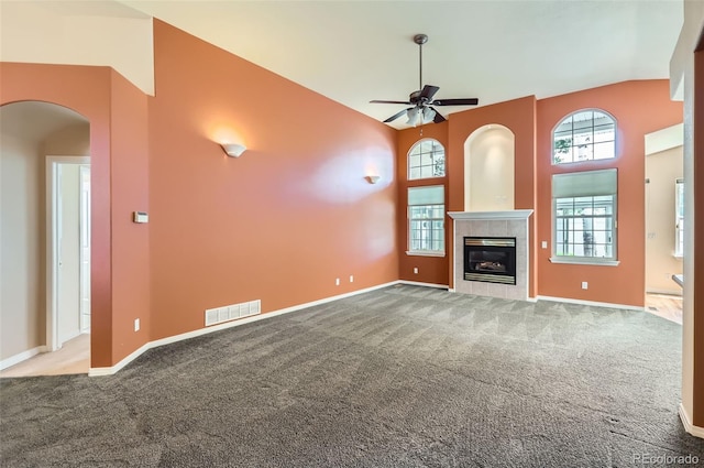 unfurnished living room featuring a ceiling fan, carpet, arched walkways, a tile fireplace, and high vaulted ceiling