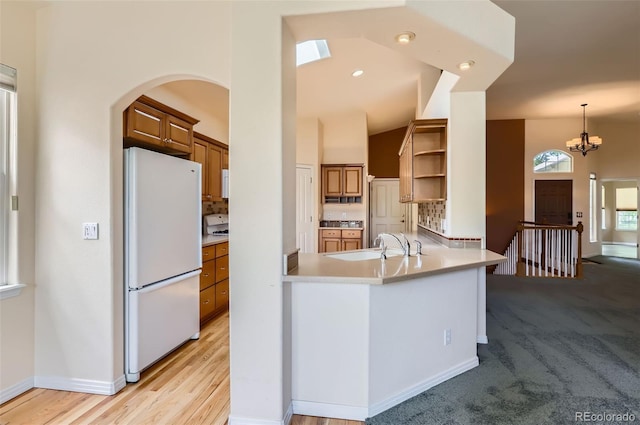 kitchen with freestanding refrigerator, open shelves, brown cabinets, arched walkways, and decorative backsplash