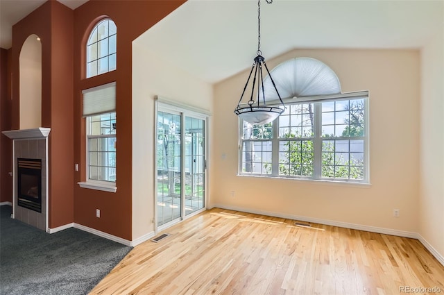 unfurnished dining area featuring wood finished floors, a tile fireplace, arched walkways, and vaulted ceiling
