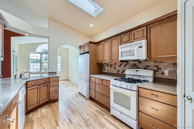 kitchen featuring white appliances, a skylight, arched walkways, light wood finished floors, and brown cabinets