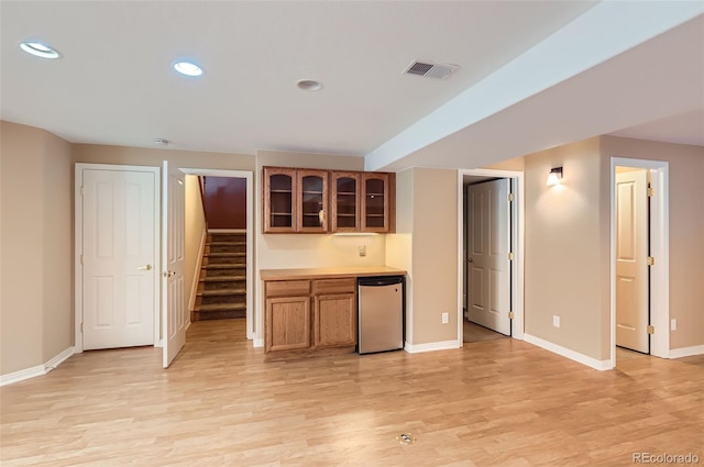 kitchen with light wood finished floors, glass insert cabinets, fridge, brown cabinets, and recessed lighting