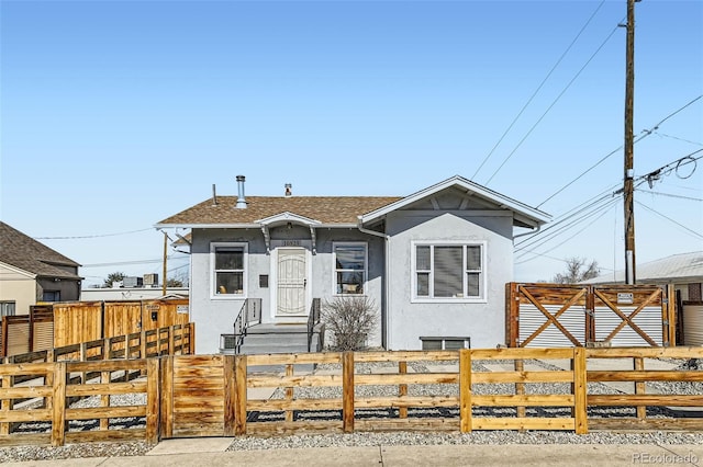 bungalow-style home featuring roof with shingles, a fenced front yard, a gate, and stucco siding