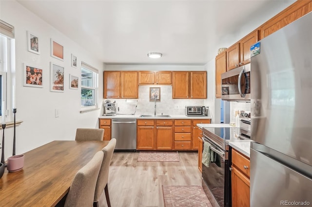 kitchen featuring light wood-type flooring, decorative backsplash, appliances with stainless steel finishes, and sink