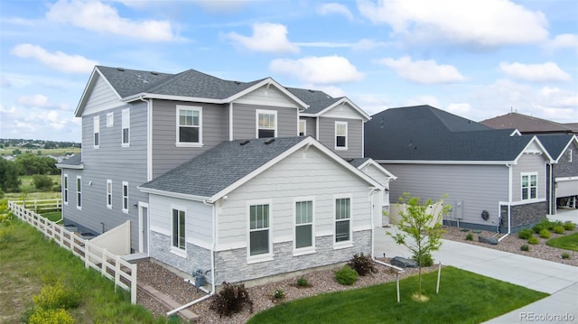 view of front of home featuring a front lawn, fence, stone siding, roof with shingles, and concrete driveway