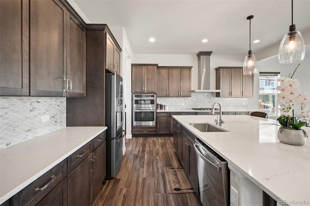 kitchen featuring wall chimney range hood, dark wood-style flooring, appliances with stainless steel finishes, a sink, and backsplash