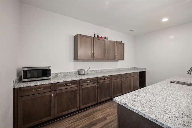 kitchen with dark brown cabinets, stainless steel microwave, dark wood-style floors, and a sink