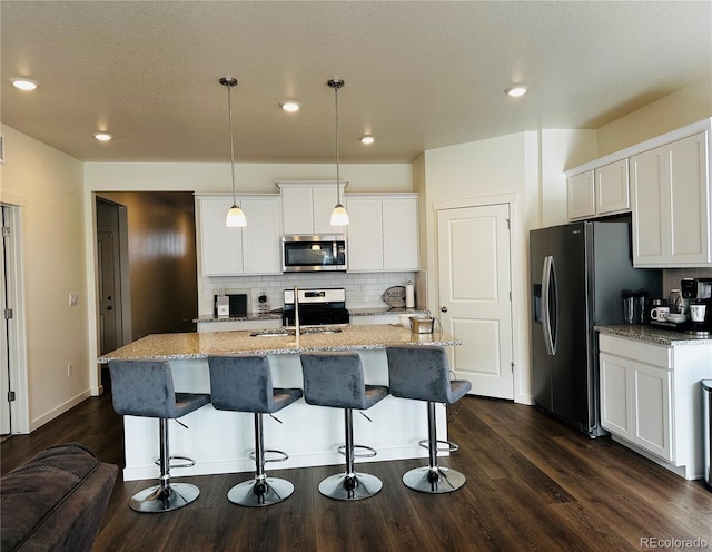 kitchen with decorative light fixtures, white cabinets, appliances with stainless steel finishes, and a kitchen island with sink