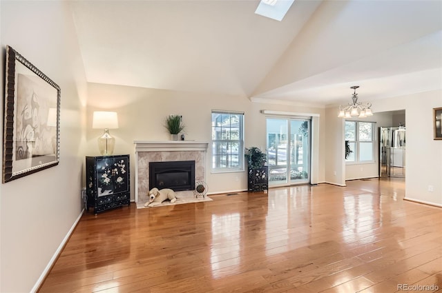 unfurnished living room with high vaulted ceiling, an inviting chandelier, a skylight, hardwood / wood-style flooring, and a tiled fireplace