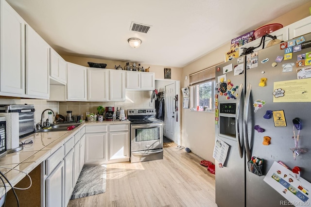 kitchen with tile countertops, light hardwood / wood-style flooring, stainless steel appliances, sink, and white cabinets