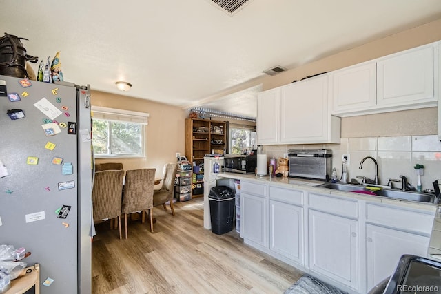 kitchen featuring decorative backsplash, white cabinets, appliances with stainless steel finishes, light hardwood / wood-style floors, and sink