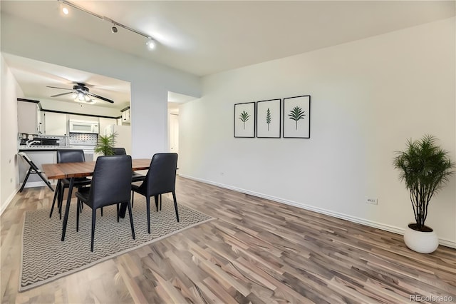 dining space featuring light wood-type flooring, rail lighting, a ceiling fan, and baseboards