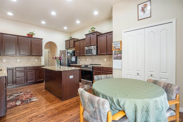 9709 Rockingham Dr, Peyton, CO 80831 - kitchen with stainless steel appliances, wood finished floors, dark brown cabinets, arched walkways, and tasteful backsplash