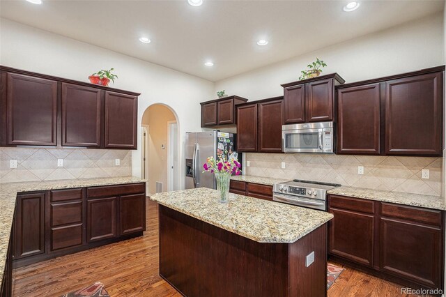 9709 Rockingham Dr, Peyton, CO 80831 - kitchen with appliances with stainless steel finishes, wood finished floors, arched walkways, tasteful backsplash, and a kitchen island